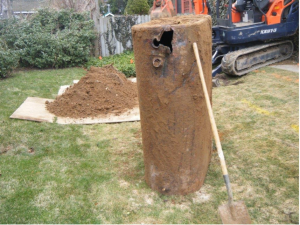 Dug up oil tank sitting vertically with a large hole visible on the top.